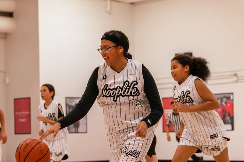 Girls in HoopLife jerseys pushing the ball up the floor on a fast break at the Regina facility