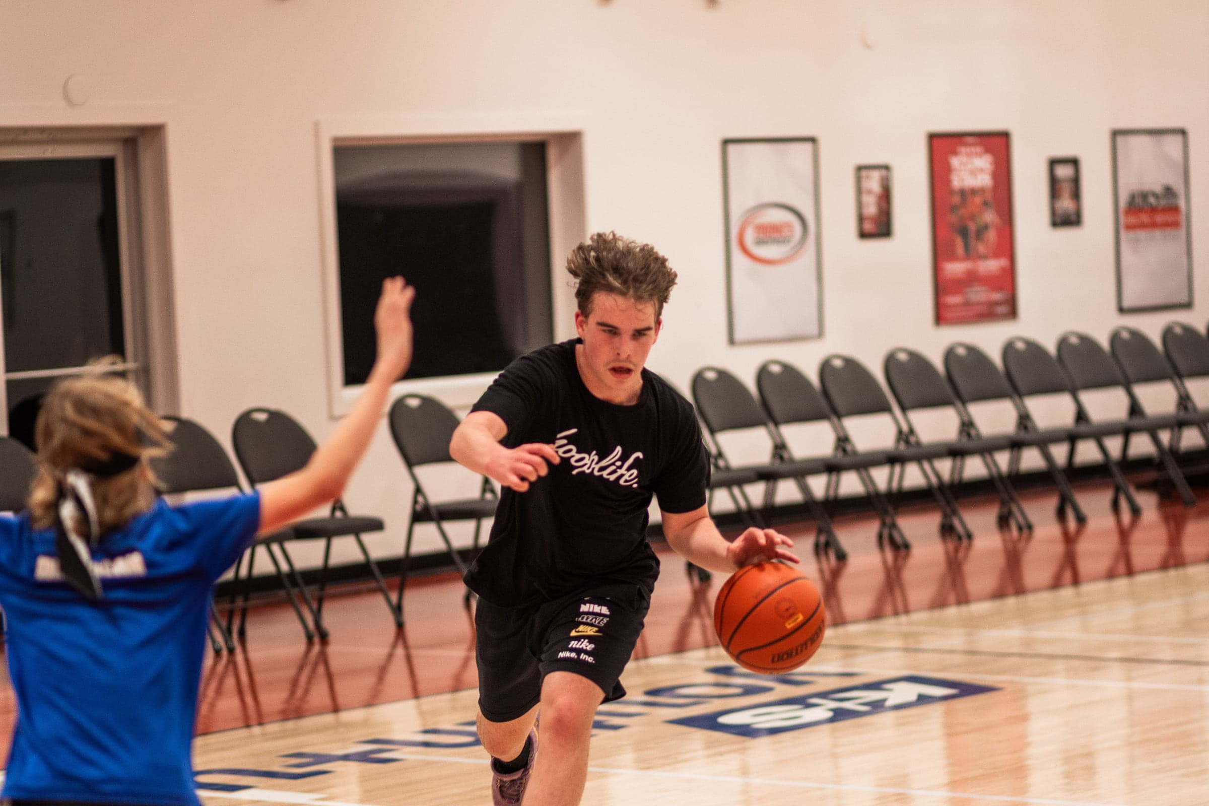 A HoopLife player driving with the ball during a game while a coach watches