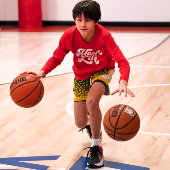 A young HoopLife player dribbling two basketballs at once in Regina