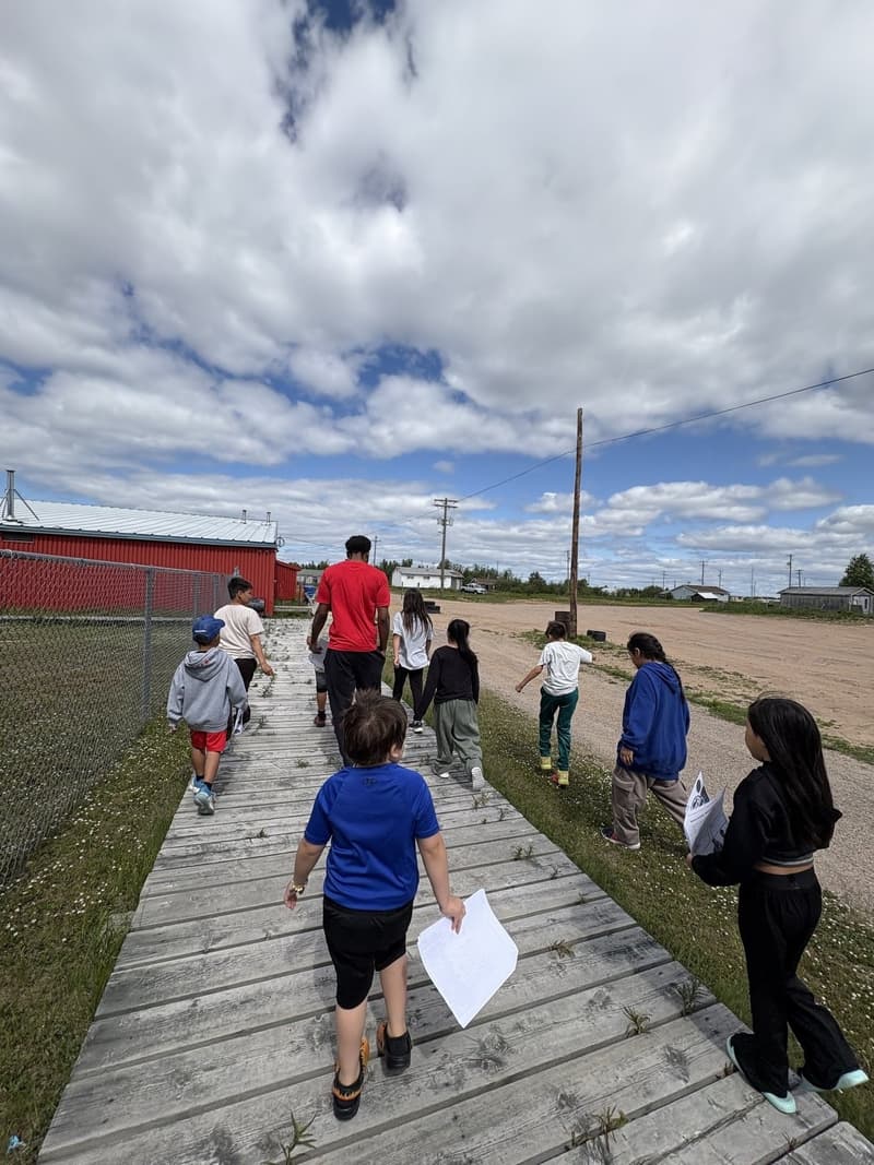 A HoopLife coach leading kids down the boardwalk in Barren Lands First Nation