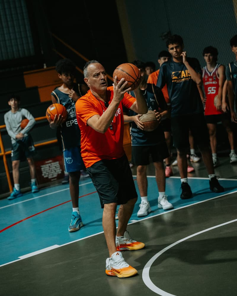 A HoopLife coach demonstrating shooting form to a circle of players in Costa Rica