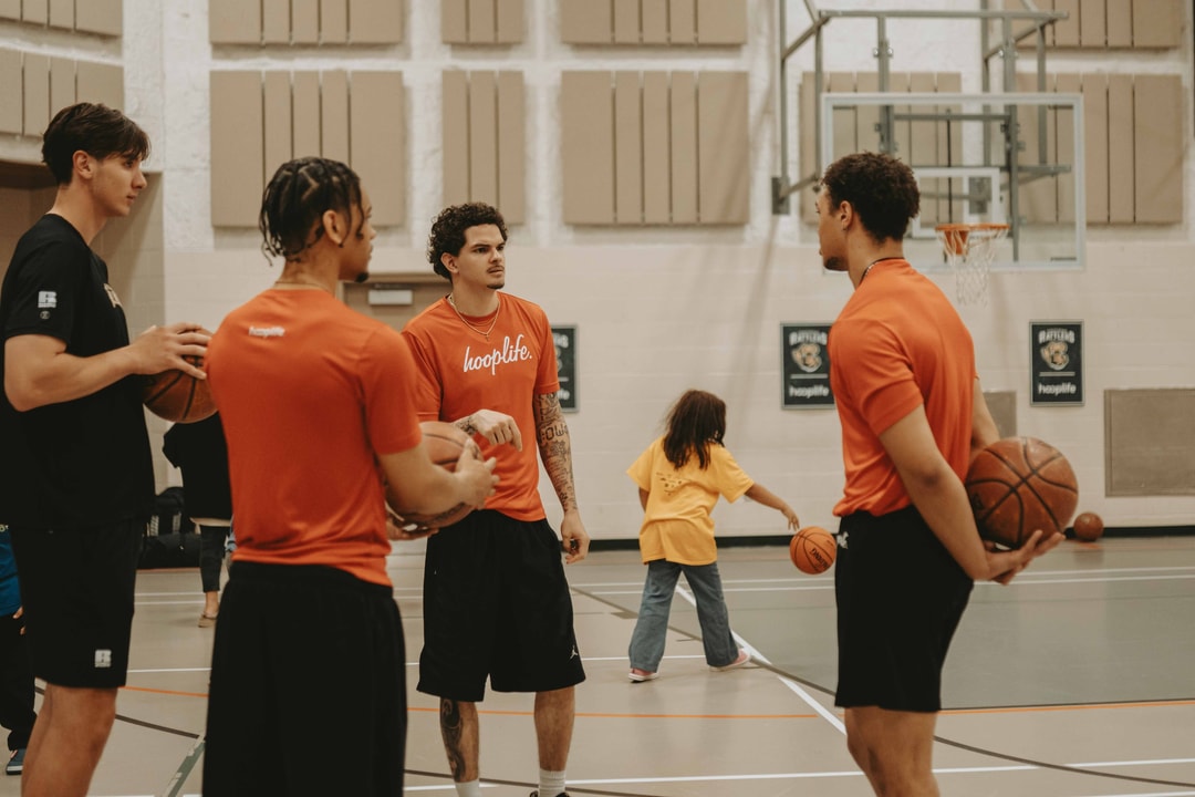 Four HoopLife coaches with basketballs on the floor at a community clinic