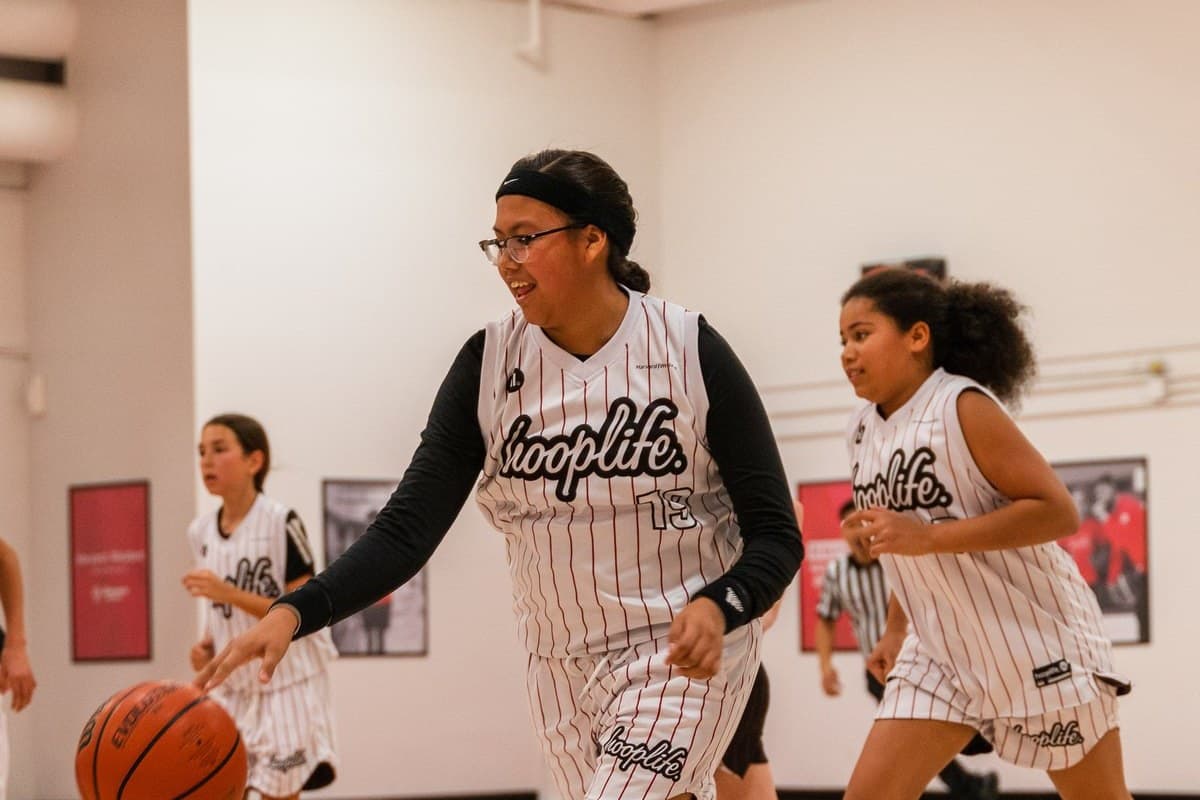 Girls in HoopLife jerseys pushing the ball up the floor on a fast break at the Regina facility