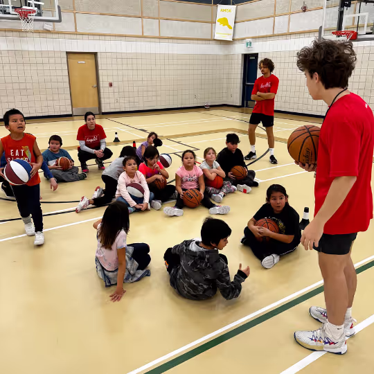 A HoopLife coach talking with a circle of seated kids