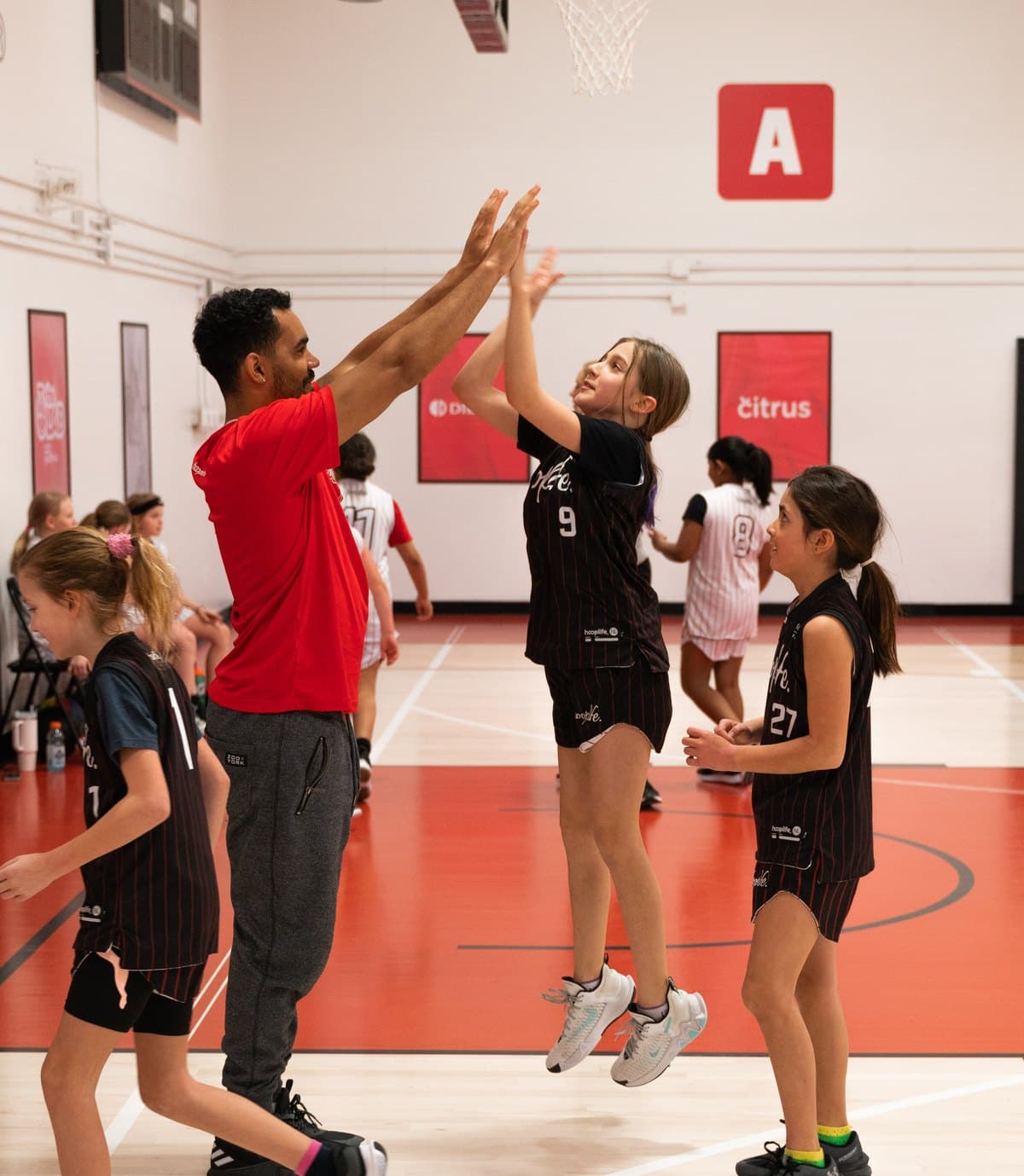 A HoopLife coach high-fiving a young player on the court at the HoopLife Centre