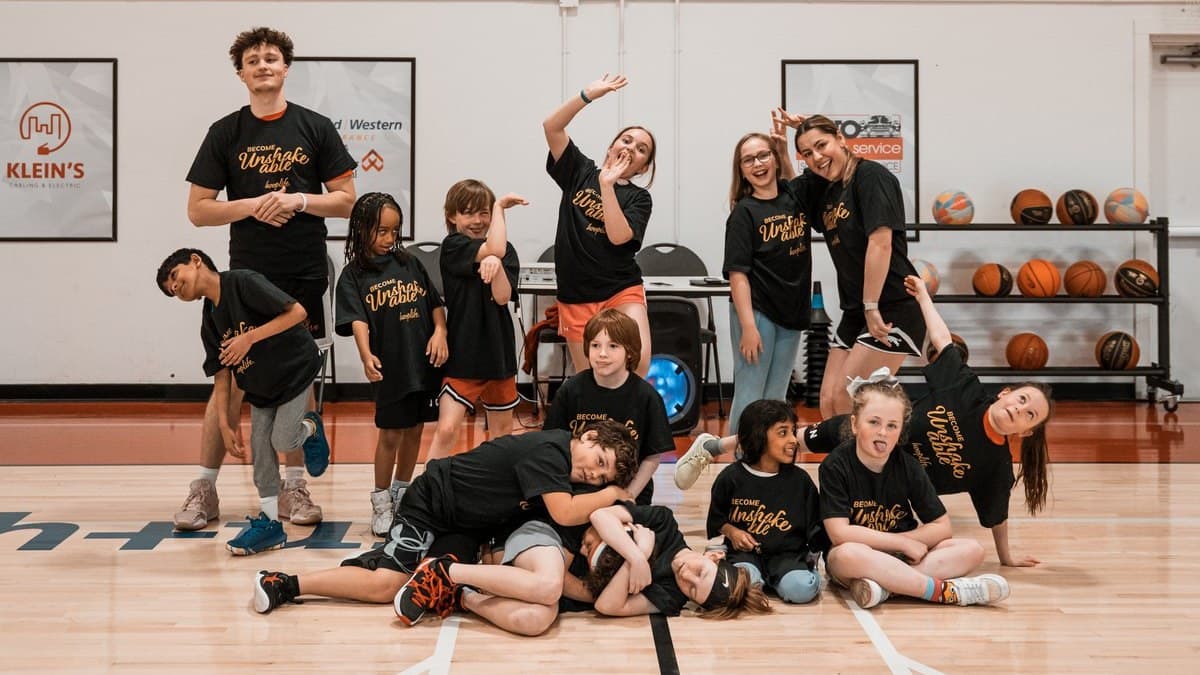 A group of HoopLife kids on the court, with partner signage on the wall behind them